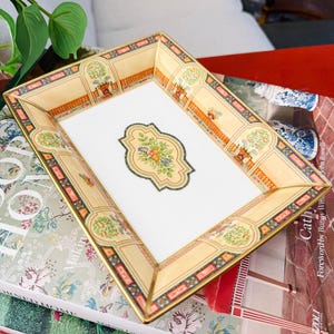 May include: A white ceramic mug with a black handle and the text "But First, Coffee" in a bold, black font. The mug is filled with a dark liquid, likely coffee, and sits on a light-colored surface.