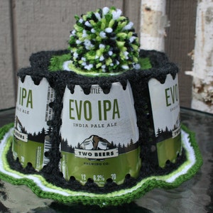 May include: A crocheted hat made from beer cans. The hat is black and green with a white pom-pom on top. The cans are labeled "Evo IPA" and "Two Beers Brewing Co."