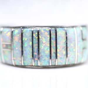 May include: A silver band ring with a white opal inlay. The opal is set in a series of vertical lines, creating a striped pattern.