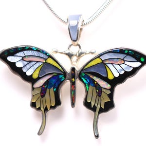 Può includere: Ciondolo a farfalla in argento con un design a mosaico colorato. Le ali presentano sezioni nere, bianche, gialle e iridescenti. Il ciondolo è appeso a una catena d'argento, creando un gioiello suggestivo.