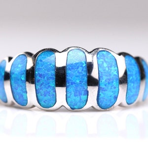 May include: A silver ring with blue opal inlay. The ring has a wavy design with multiple bands of opal.