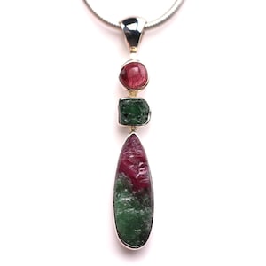 May include: A silver pendant necklace featuring three natural gemstones. The pendant has a round, a square, and a teardrop-shaped stone in shades of red and green. The necklace has a silver chain.