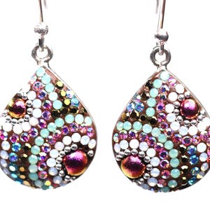 May include: A pair of teardrop-shaped earrings with a silver hook. The earrings are covered in a mosaic of small, colorful crystals in shades of pink, purple, white, blue, and gold. The crystals are arranged in a dense pattern, creating a sparkling effect.