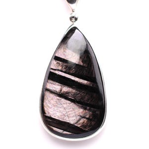 May include: A teardrop-shaped pendant with a silver-colored bail. The pendant features a polished, dark gemstone with black and silver-colored striations. The gemstone is set in a silver-colored bezel.