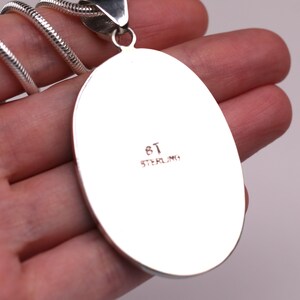 May include: A silver oval pendant with the inscription "8T STERLING" on the back.