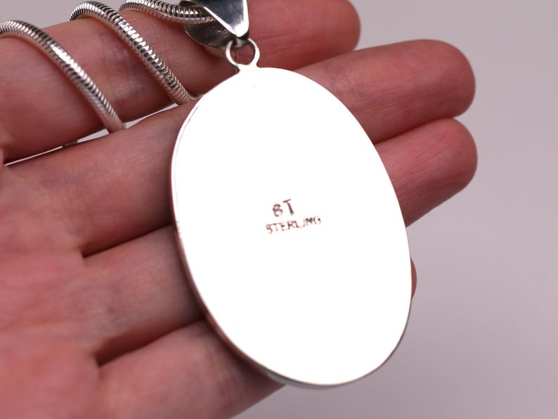 May include: A silver oval pendant with the inscription "8T STERLING" on the back.