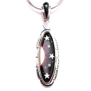 May include: Silver pendant necklace with an oval pendant. The pendant features a black background with a white crescent moon, three white stars, and red and colorful accents. The pendant is approximately 1.5 inches long.