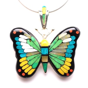 May include: A butterfly pendant with a silver chain. The pendant features a colorful mosaic design with black, turquoise, yellow, green, and white elements. The butterfly's wings are detailed with various shapes and colors.