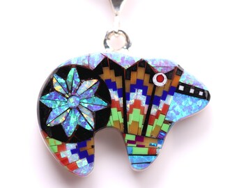 Puede incluir: Un colgante de oso de mosaico azul, verde, rojo y negro con una anilla de plata. El oso está hecho de pequeñas piezas de ópalo y otras piedras preciosas.