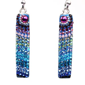 May include: A pair of rectangular dangle earrings. Each earring is covered in a gradient of colorful rhinestones, transitioning from dark blue to light blue, with accents of pink, purple, and clear stones. A silver-tone hook is at the top.