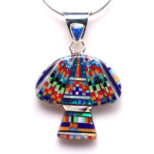Könnte beinhalten: Ein pilzförmiger Anhänger mit einer Silberkette. Der Anhänger hat ein Mosaikdesign mit blauen, roten, orangen, grünen und weißen Teilen. Oben ist ein kleiner blauer Stein eingesetzt. Ein einzigartiges Schmuckstück.