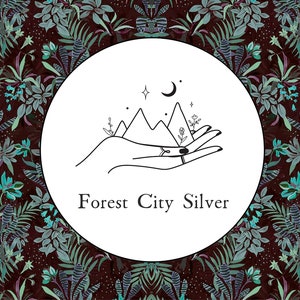 May include: A black and white illustration of a hand holding a mountain range with a crescent moon and stars above. The text "Forest City Silver" is below the illustration.