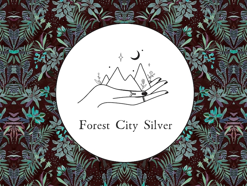 May include: A black and white illustration of a hand holding a mountain range with a crescent moon and stars above. The text "Forest City Silver" is below the illustration.