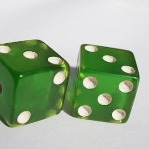 May include: Two green dice with white dots. The dice are made of glass and have a translucent appearance.
