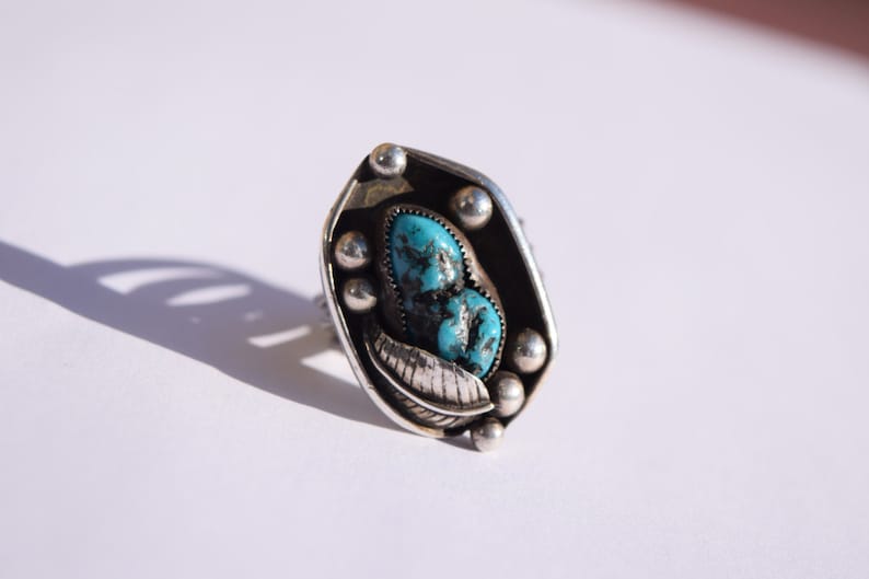 Puede incluir: Un anillo de plata con una piedra turquesa engastada en un dise&ntilde;o de hoja.
