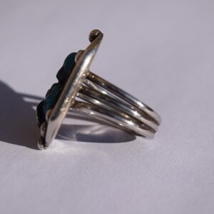 Puede incluir: Un anillo de plata con una piedra turquesa engastada en un dise&ntilde;o geom&eacute;trico. El anillo tiene una banda ancha con m&uacute;ltiples bandas.
