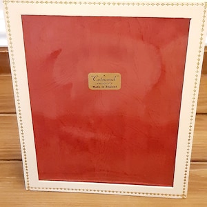Könnte beinhalten: Ein weißer Bilderrahmen mit goldener Verzierung und einem roten Passepartout. Der Rahmen trägt ein Etikett mit der Aufschrift "A Cotswood Product Made in England".