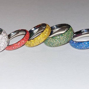 May include: Set of seven sparkly rings in various colors, including white, red, yellow, green, blue, and pink. The rings are made of metal and have a textured surface.