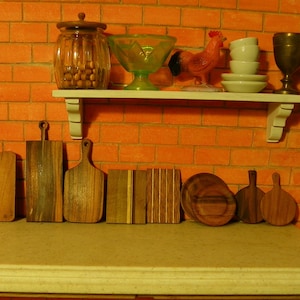 May include: A set of nine wooden cutting boards of various sizes and shapes, arranged on a white countertop. The boards are made of different types of wood, including maple, walnut, and cherry. The boards are all in good condition and have a natural finish.