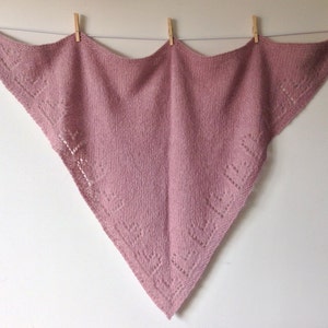 May include: A delicate pink knitted shawl with a lacy pattern around the edges.