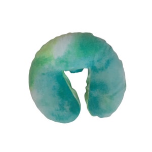 May include: A green and blue tie-dye travel neck pillow. The pillow is shaped like a horseshoe and has a hole in the center for the neck.