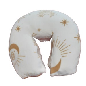 May include: White neck pillow with a gold celestial pattern featuring moons, stars, and sunbursts.