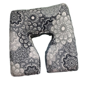 May include: A gray and white patterned travel pillow with a U-shaped opening for the head. The pillow is made of soft, plush fabric.