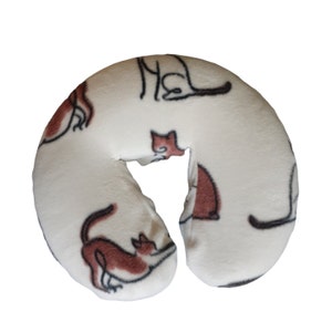 May include: White fleece neck pillow with a brown cat print. The pillow is shaped like a horseshoe and is designed for use during massage therapy.