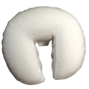May include: A white, U-shaped massage table face cradle cushion. The cushion is made of a soft, plush material and has a curved design to support the face during massage or spa treatments. The cushion is designed to provide comfort and relaxation.