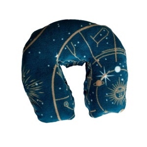 May include: A dark teal travel neck pillow with a celestial design. The pillow features a pattern of gold constellations, stars, and a sun and planet design. The U-shaped pillow is made of soft fabric.
