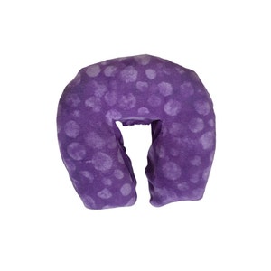 May include: Purple neck pillow with a white polka dot pattern. The pillow is designed to support the head and neck during a massage.