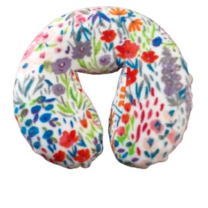 May include: U-shaped travel pillow with a white background and a colorful floral pattern. The pattern includes red, blue, purple, and orange flowers with green leaves. The pillow is designed for neck support and comfort.