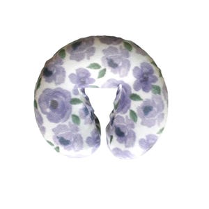 May include: A U-shaped travel pillow with a floral pattern. The pillow features a white background with lavender flowers and green leaves. The pillow is designed for neck support and comfort.