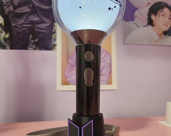 May include: A black and purple BTS light stick with a clear, glowing orb. The orb has text that reads "RUNSEOKJIN EP TOUR" and "BTS". A green accent sits atop the orb. A gray strap with "ARMY" is visible.