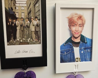 May include: Two framed photos with purple glitter hearts hanging below. The photo on the left shows a group of seven people, with the text "Life Goes On" written below. The photo on the right shows a man with pink hair, and the text "RM" is on the heart below.
