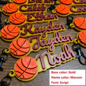 May include: Keychains with personalized names and basketball designs. The base is gold, the name is maroon, and the font is script. Each keychain has a basketball and a clasp.