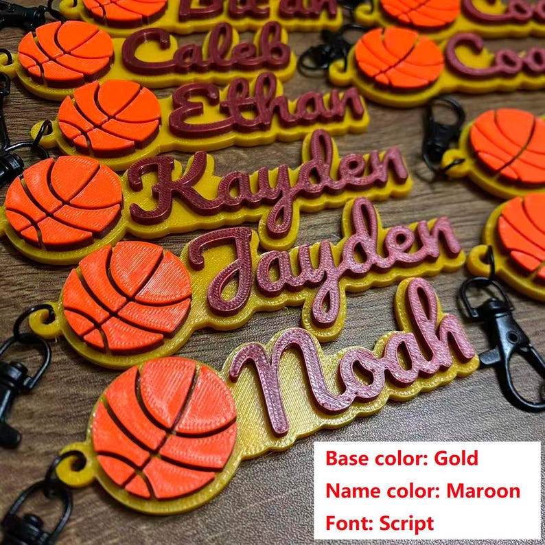 May include: Keychains with personalized names and basketball designs. The base is gold, the name is maroon, and the font is script. Each keychain has a basketball and a clasp.