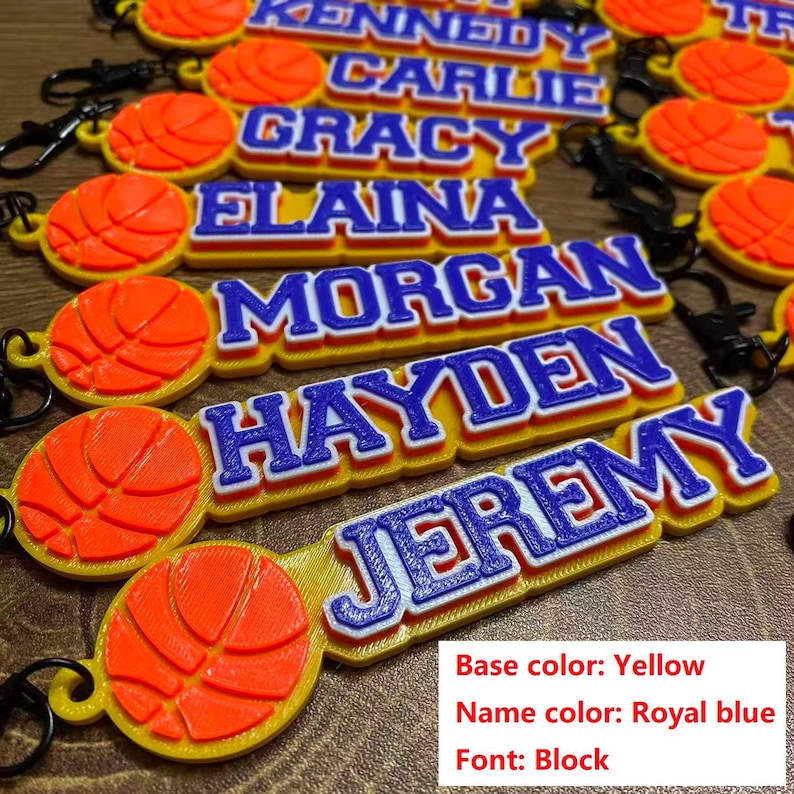 May include: Yellow keychains with names in royal blue block letters and a 3D orange basketball design. The names include: Kennedy, Carlie, Gracy, Elaina, Morgan, Hayden, and Jeremy. The base color is yellow, the name color is royal blue, and the font is block.