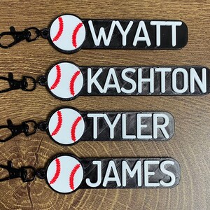 May include: Four black and white baseball-themed keychains with a white baseball and red stitching. Each keychain has a black name tag with white lettering. The names are Wyatt, Kashton, Tyler, and James.