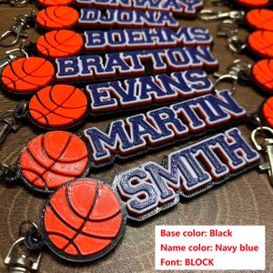 May include: Basketball-themed keychains with personalized names in navy blue block letters. Each keychain features an orange basketball design. The base color is black. The image includes the names DJONA, BOEHMS, BRATTON, EVANS, MARTIN, and SMITH.