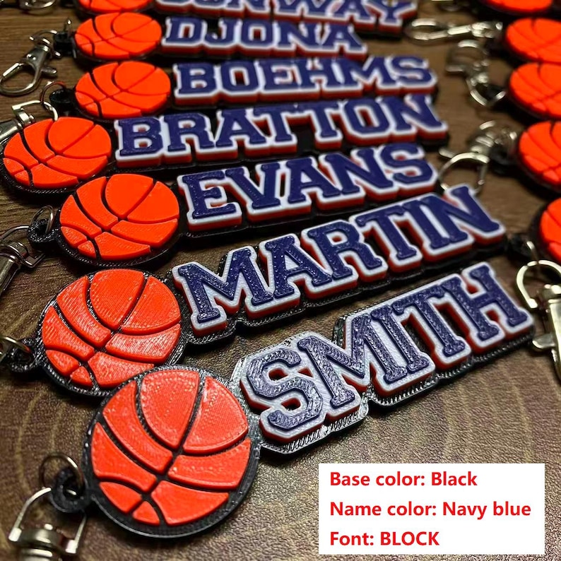 May include: Basketball-themed keychains with personalized names in navy blue block letters. Each keychain features an orange basketball design. The base color is black. The image includes the names DJONA, BOEHMS, BRATTON, EVANS, MARTIN, and SMITH.