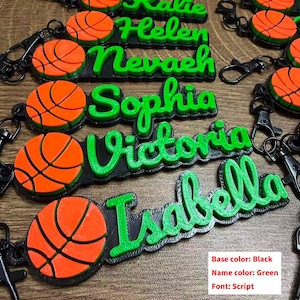 May include: Custom basketball keychains with names in green script font. Each keychain features a black base and an orange and black basketball design. The names include Helen, Nevaeh, Sophia, Victoria, and Isabella.