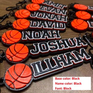 May include: Basketball-themed keychains with personalized names in black and white block lettering. Each keychain features a 3D-printed orange basketball. The base color is black, and the name color is black.