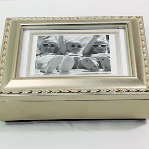 May include: Silver-toned photo frame music box with a black and white photo of three children wearing sunglasses and flip-flops. The photo frame has a decorative border.