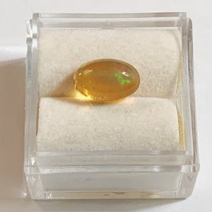 May include: A yellow oval opal gemstone with green and orange flashes of color, displayed in a white velvet-lined box.