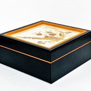 May include: Black wooden box with a gold trim and a clear glass top. The top features a pressed flower design.