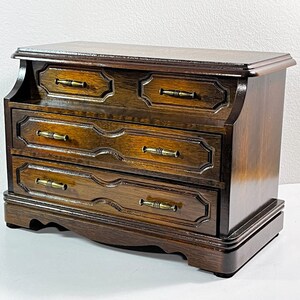 May include: A dark wood jewelry box with four drawers and brass pulls. The box has a curved front and a slightly raised top.
