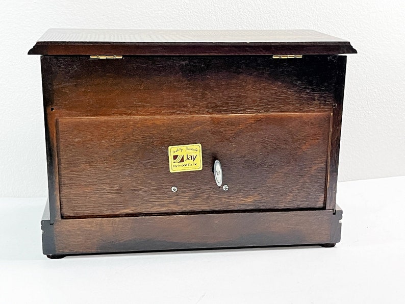 May include: A dark brown wooden music box with a hinged lid and a gold label that reads "Quality Products Jay Instruments UK".
