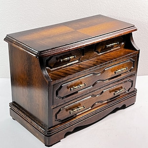 May include: A dark wood jewelry box with three drawers and brass hardware. The top of the box has a decorative inlay.