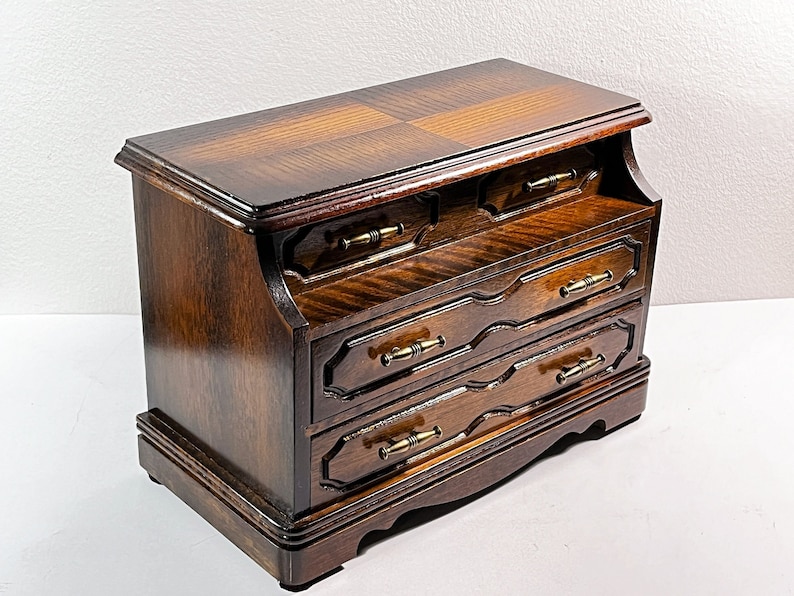 May include: A dark wood jewelry box with three drawers and brass hardware. The top of the box has a decorative inlay.